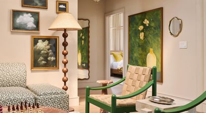 A creatively decorated suite with framed artworks, an eye-catching upholstered couch in black and white, floral patterns, rattan and wood beige and green chairs, and a tall, standing bobbin lamp.