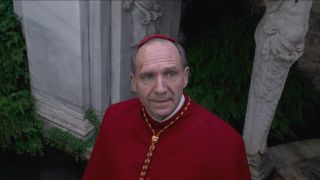 Ralph FIennes smiles wearily as he looks to the sky in the garden in Conclave.