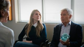 Two people (Lily Rabe as Meg, center, and Harrison Ford as Paul, right, holding a water bottle), sit on a couch and talk to a doctor (left) in an office, in 'Shrinking.'