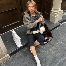 vivian wears capris and a light jacket with flats and socks while sitting on a stoop