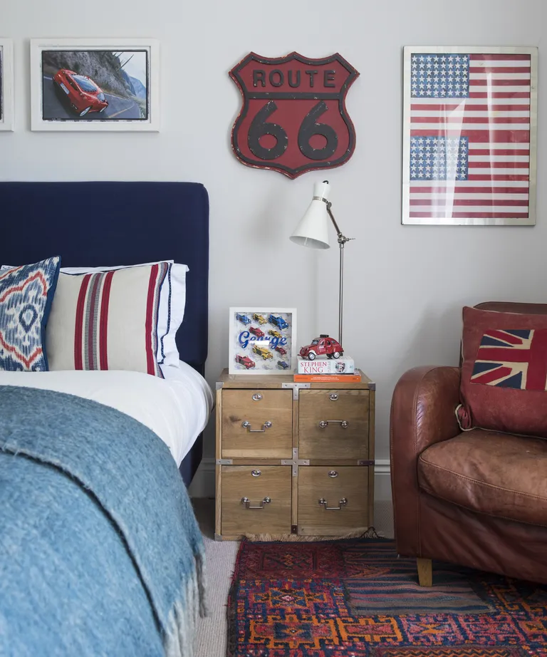 A bedroom with red and blue furnishings and artwork, with an aged leather armchair