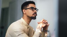A man appears thoughtful as he looks into the distance in his office. 