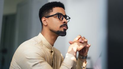 A man appears thoughtful as he looks into the distance in his office. 
