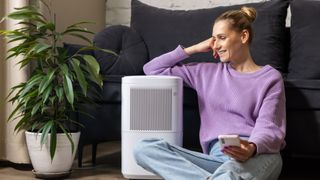 Woman sitting beside portable air conditioner, holding phone