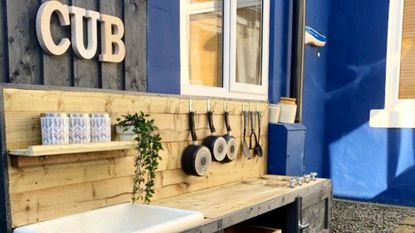 DIY mud kitchen built with wood, against a cobalt blue wall