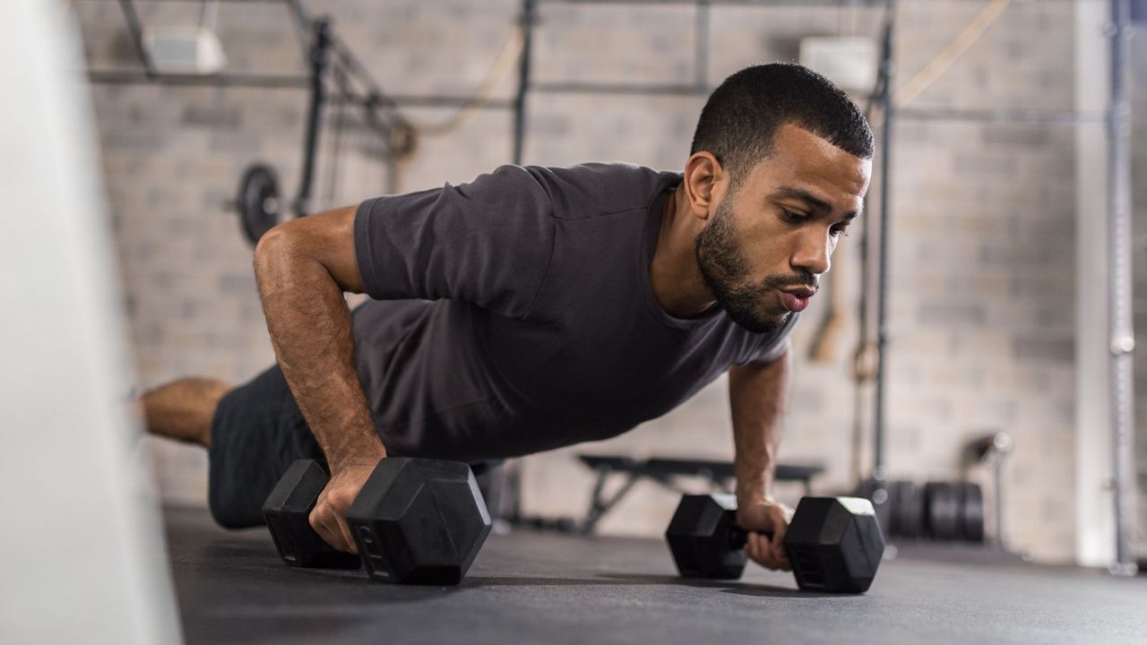 A man performing a devil press with dumbbells