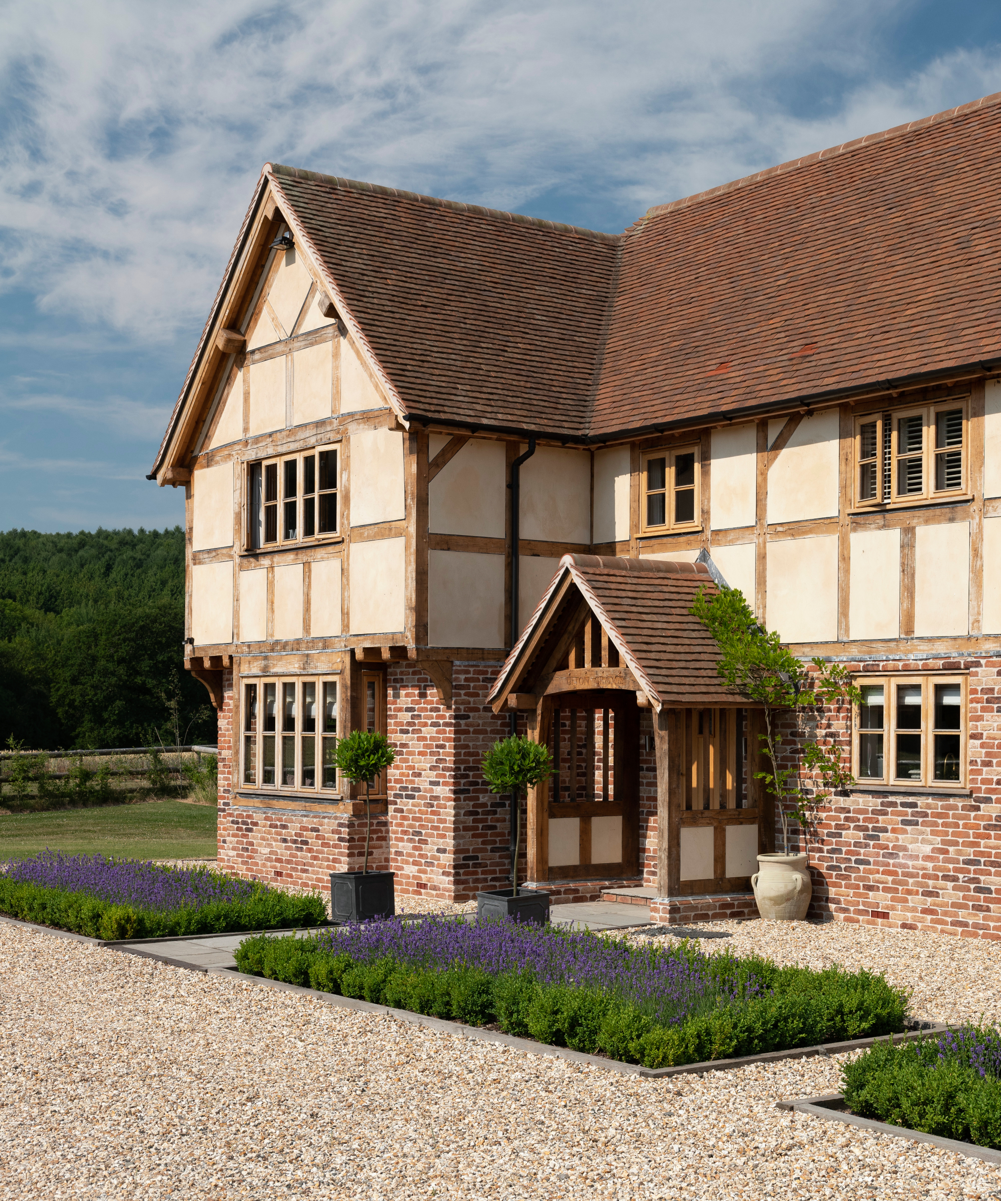 oak frame porch with pitched tiled roof, side panels with oak struts and infil panels on brick and oak home with lavender planted flower beds set into gravel drive and entrance