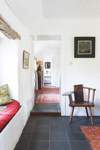 Hallway in a coastal home, with slate tiles, red rugs, window seat and antique pipe and pint chair