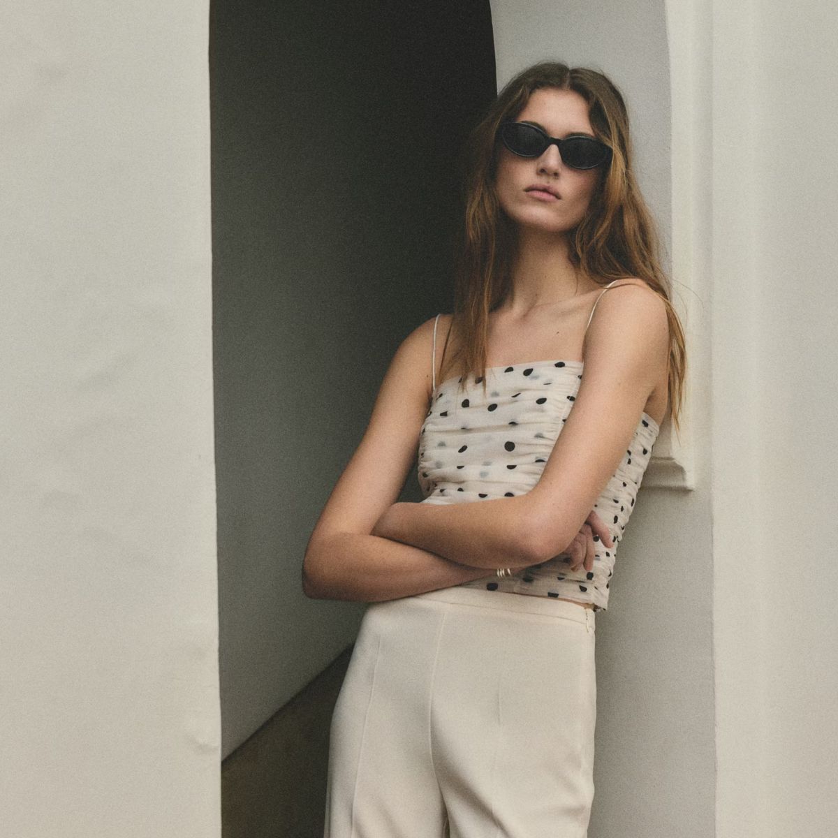 Woman wears polka dot top, cream trousers and sunglasses