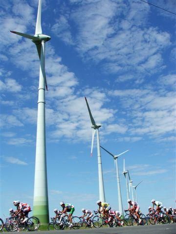 Riders spin past a wind farm