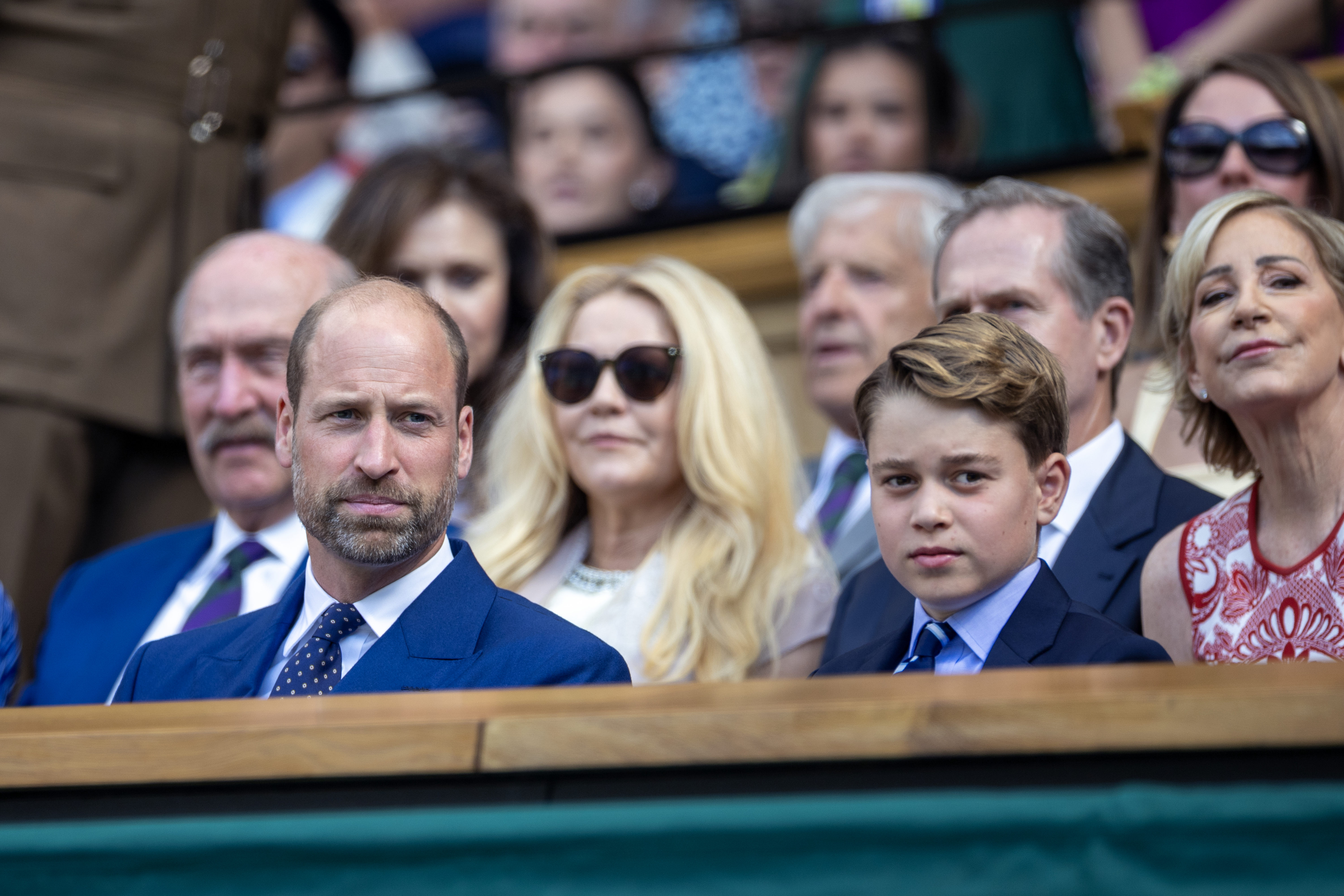 Prince George and Prince William sitting next to each other in blue suits at Wimbledon
