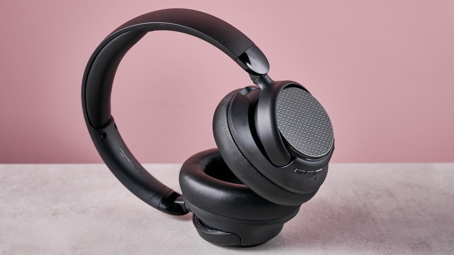 Amazon Basics Hybrid Active Noise Cancelling Headphones on a gray surface, with a pink background