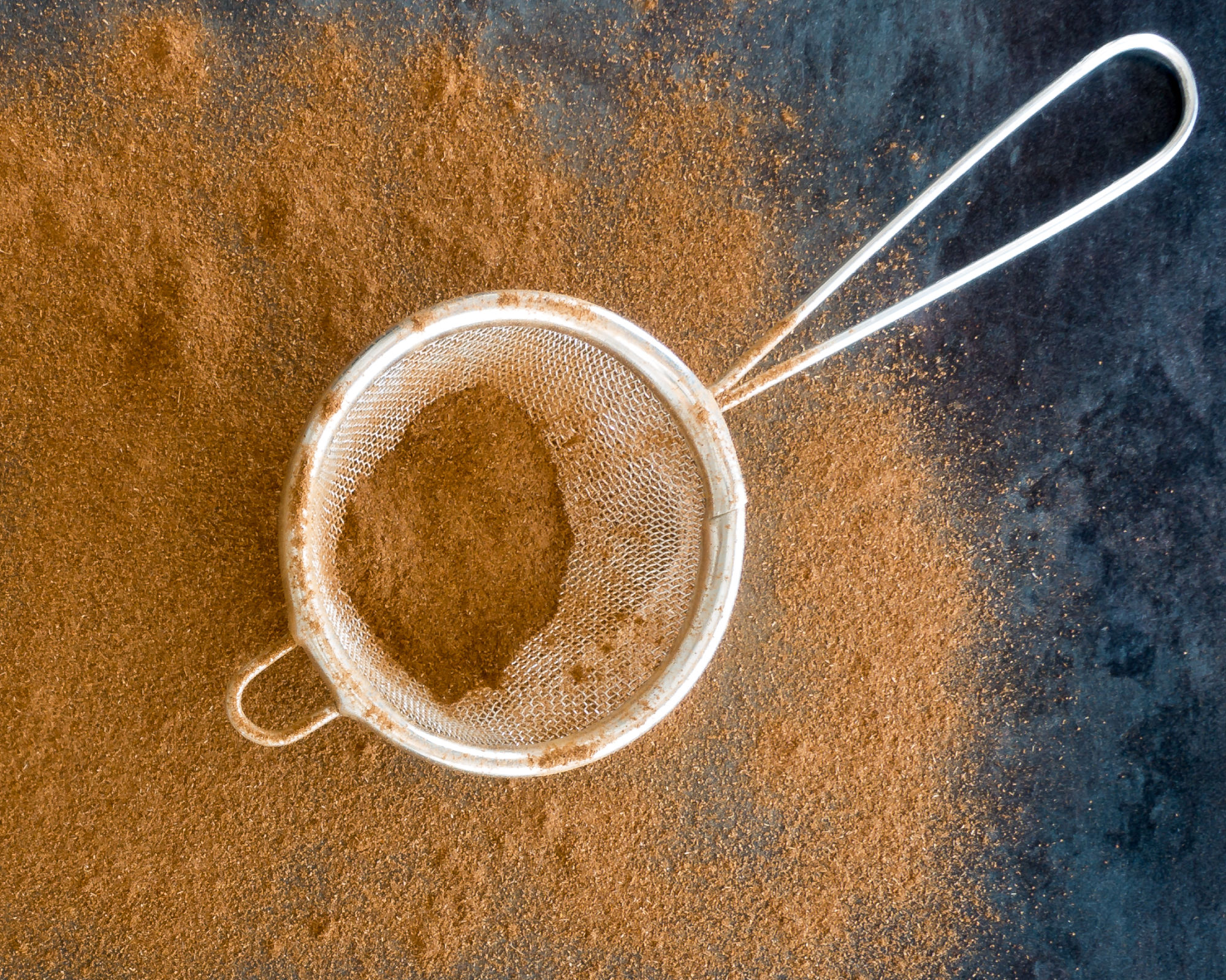 small sieve being used to lightly dust surface with cinnamon powder