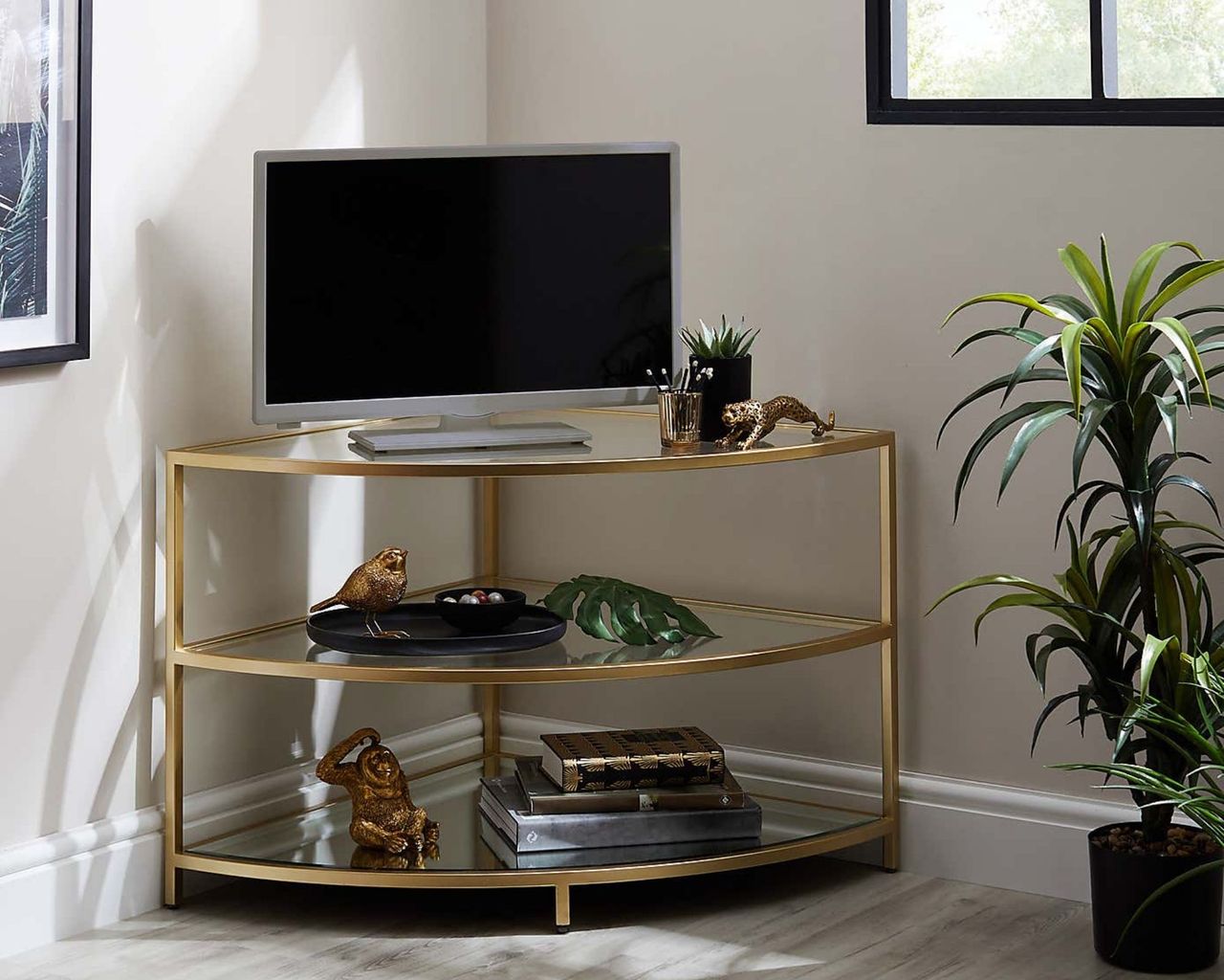 Claudia Gold Effect Corner TV Stand decorated with accessories next to plant