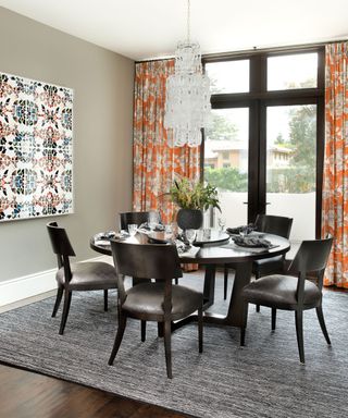 Gray dining room with orange patterned curtains, round black dining table and chairs, artwork on walls