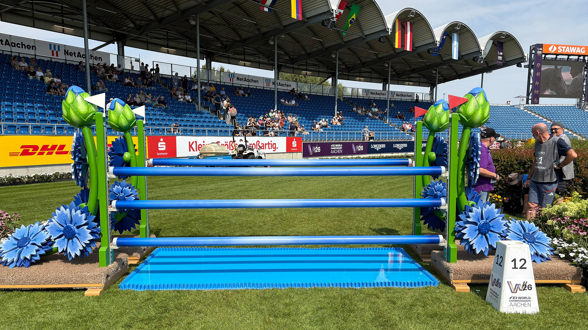 A blue oxer showjump over a bright blue water tray heading towards the crowd in the main arena at Aachen