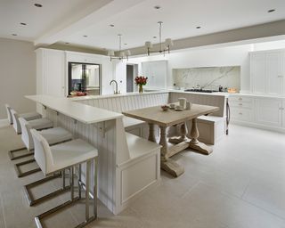 Breakfast bar ideas incorporated into white banquette seating in a large, all-white kitchen with wooden dining table.