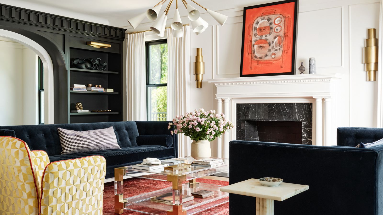 Living room with marble fireplace, pink rug, glass coffee table, black bookcase and abstract art