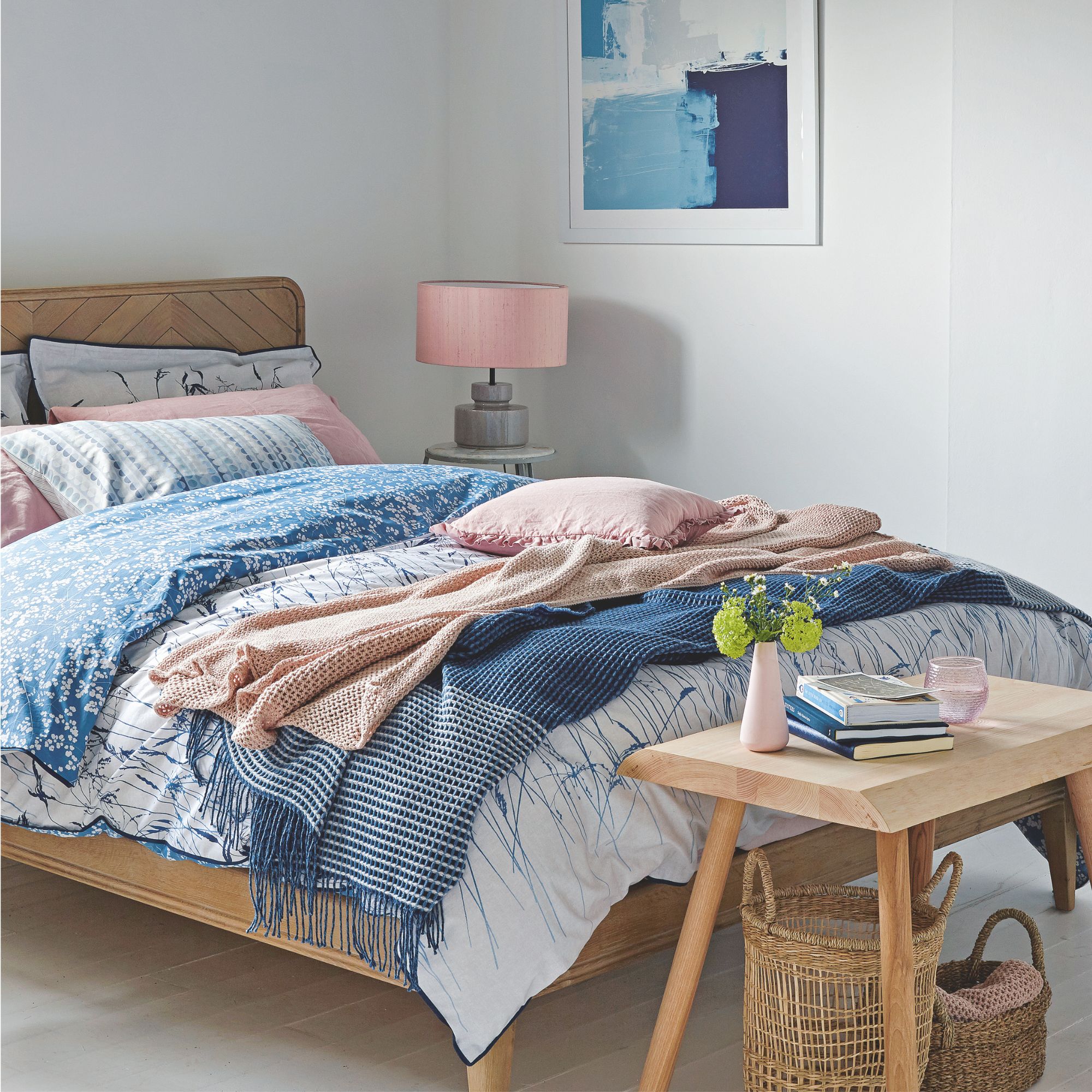 A white bedroom with a made bed in the middle, with blue and pink bedding