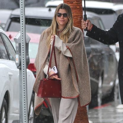 Sofia Richie Grainge wearing a leather trimmed cape, ribbed kit pants, and a burgundy handbag