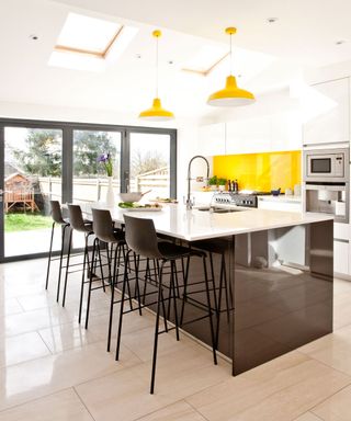 open plan kitchen with yellow splash back and yellow lights with aluminium doors leading to the outside garden