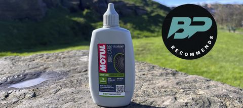 Motul Chain Lube Dry bottle on stone with field behind