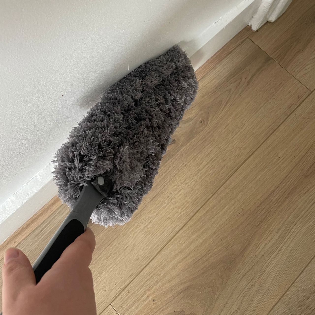 Using a grey feather duster to dust white skirting boards