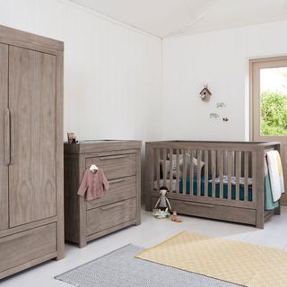 Grey cot, drawer chest and wardrobe in children's room with white wallpaper