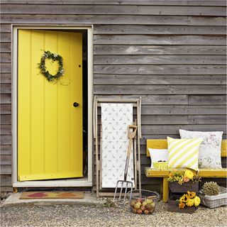 yellow front door with grey wooden wall and bench with cushions