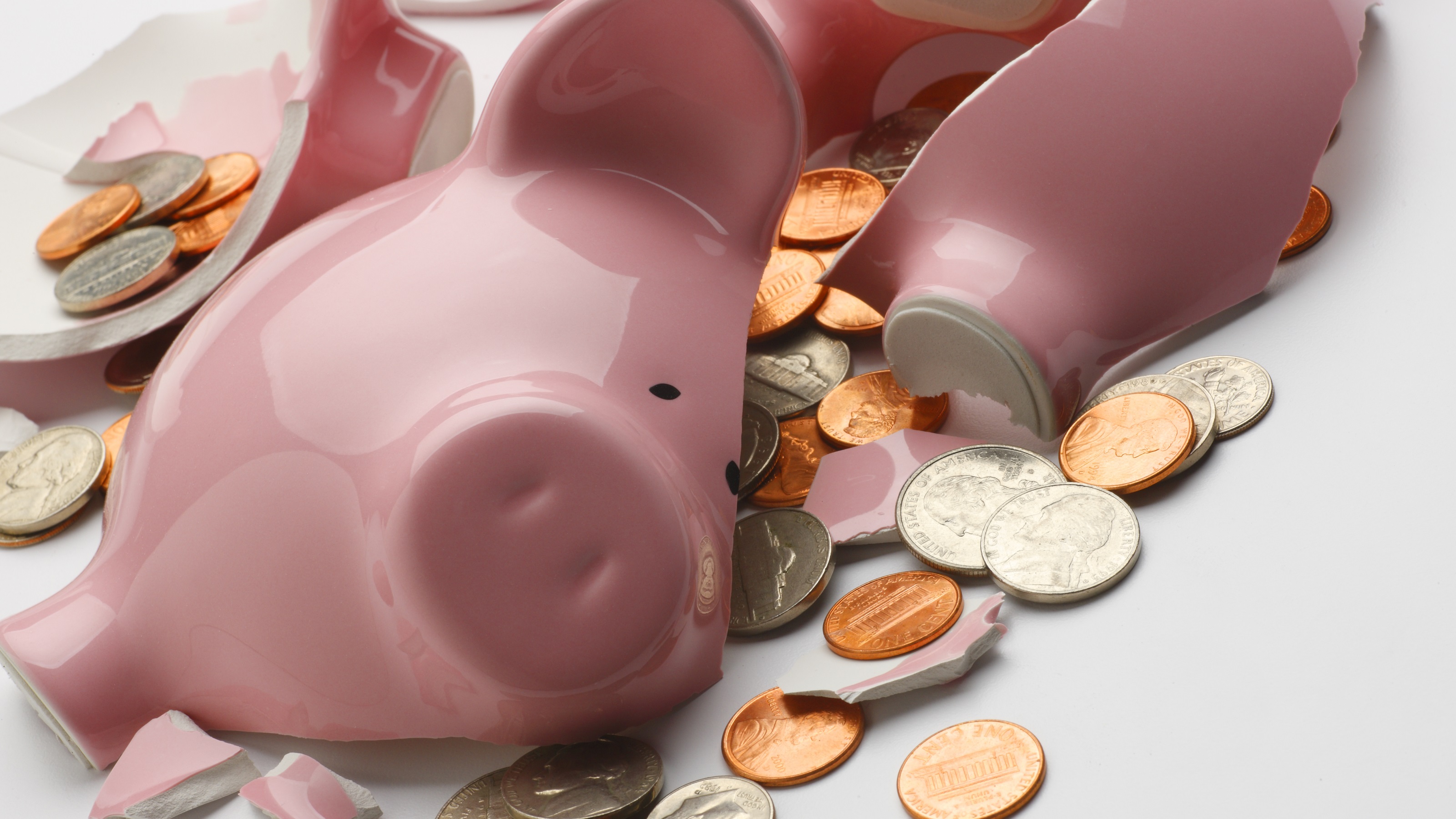 A broken piggy bank's pieces are scattered among coins.