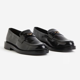 Cutout of shiny black loafers from H&M against a pale background