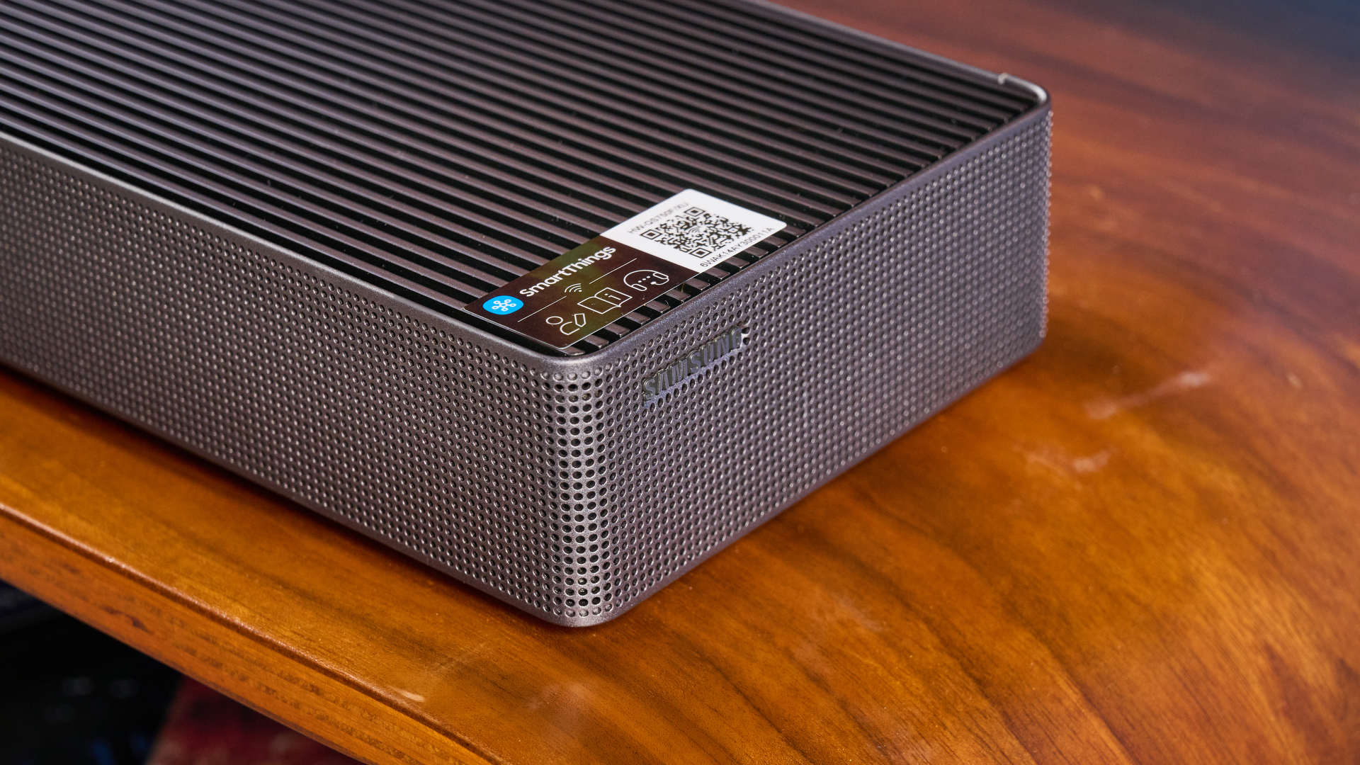 the samsung qs750f soundbar with two rear surround speakers and subwoofer photographed against a blue background and a TV