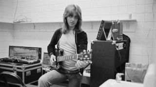 Joey Molland in a backstage dressing room with guitar