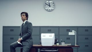 Mark Scout sits on the edge of a Lumon desk with a plaster on his head in Severance season 1