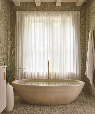 bespoke curved concrete bathtub in stone room with linen curtain