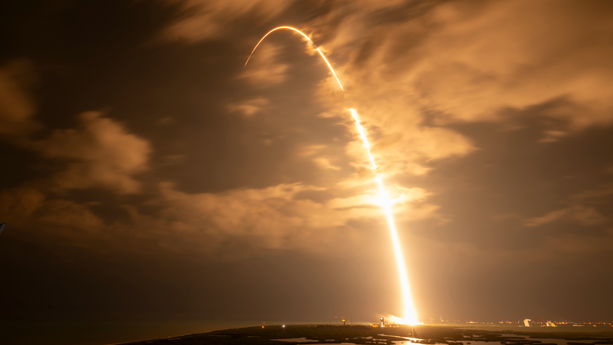 A rocket launch carves an orange arc into a dark night sky in this long-exposure photo.