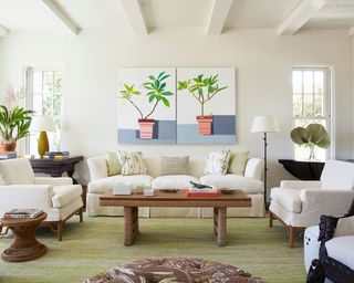 White living room with pastel green flooring, wood coffee table and row of three art prints above sofa
