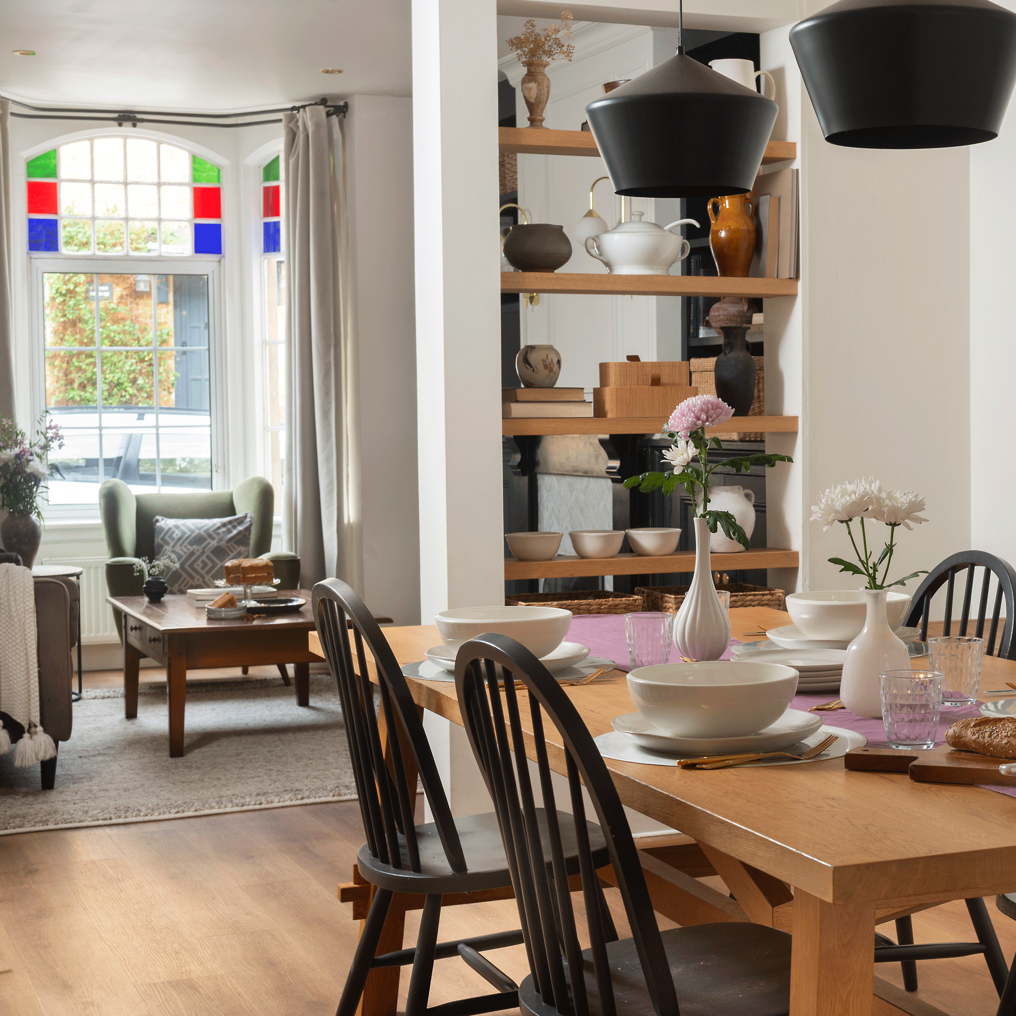 an open plan living and dining area with an open bookcase room divider and stained glass window