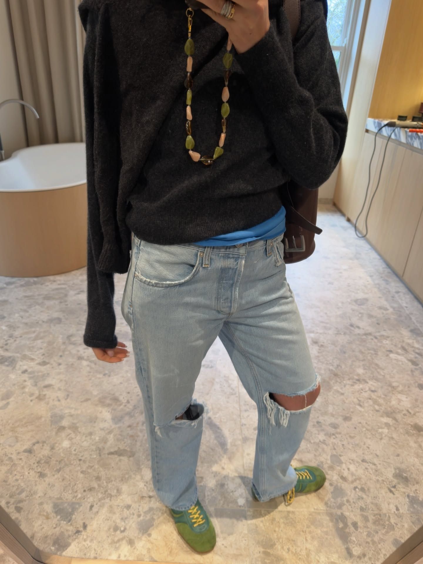 She wears ripped jeans with green sneakers and a gray sweater.