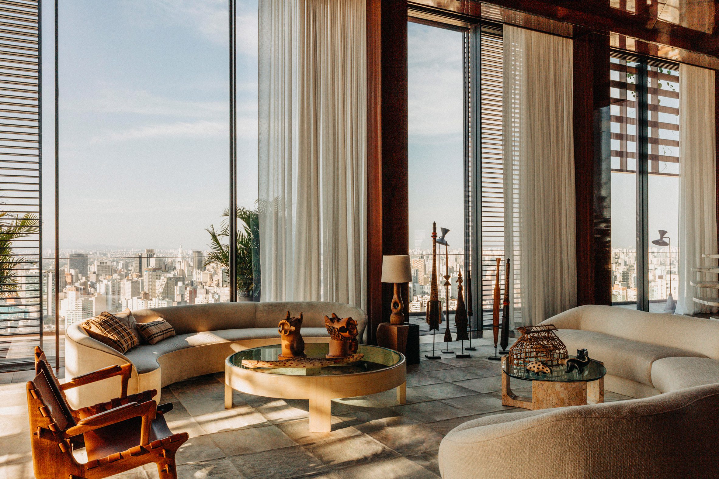A spectacular, sun-filled penthouse blends Brazilian heritage with sleek surfaces, sculptural furniture, and researched artwork, also incorporating greenery into an earthy scheme.