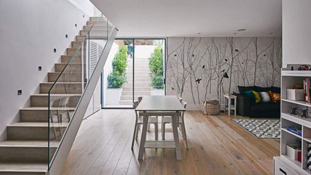 A white basement with glass staircase railing, light wooden flooring and white dining area with white walls and feature wall decor