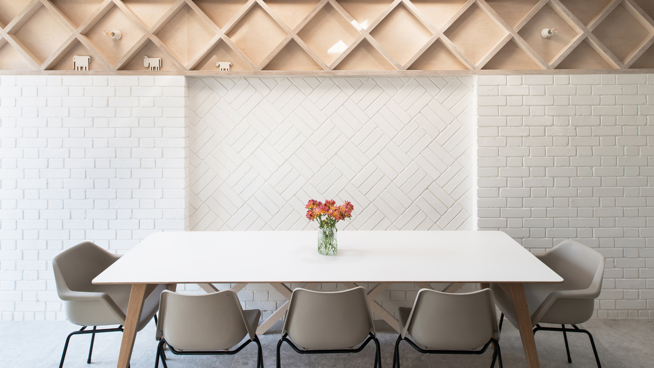 a dining table with chairs. In this extension there is a brick wall painted white with different birck layout patterns and above it a contrasting wooden wall/ ceiling