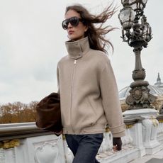 Woman wears taupe funnel-neck jacket, blue jeans 