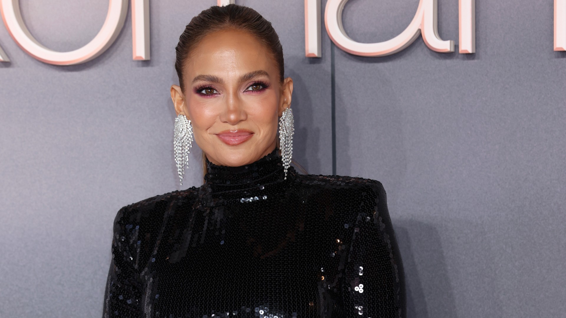 jennifer lopez attends a film premiere wearing a black gown and poses in front of a gray background