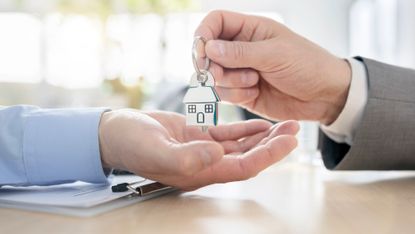 Close up of hands exchanging house shaped keychain in an office