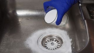 baking soda being sprinkled around a drain hole in a sink
