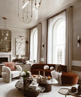 neutral living room with curved chestnut sofa, white curved chair, statement pendant and arched windows
