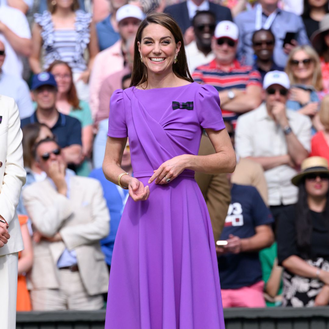 Kate Middleton wearing a bright purple dress and smiling with a crowd of fans behind her at Wimbledon