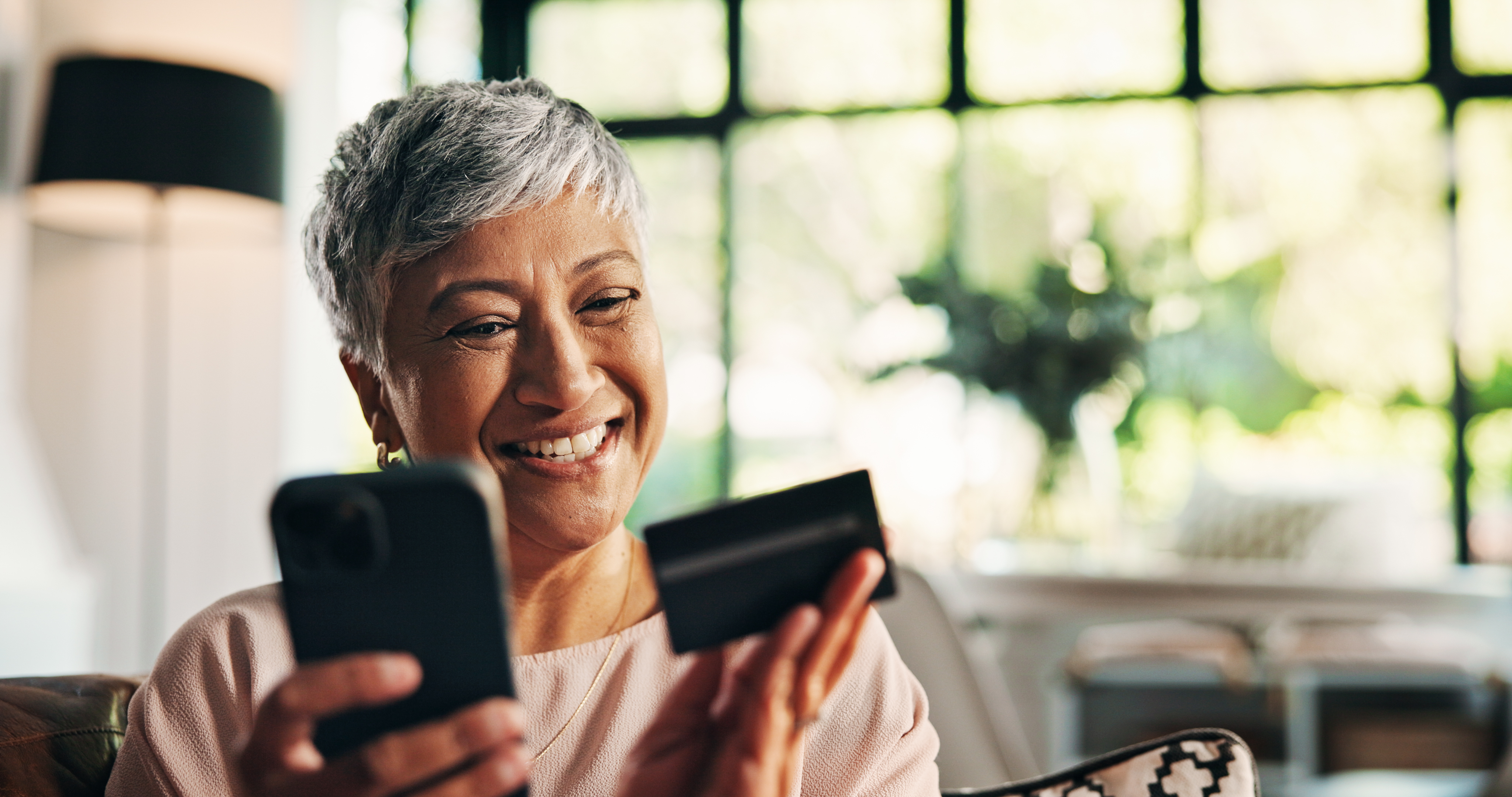 a cheerful woman examining her credit card while holding her smartphone