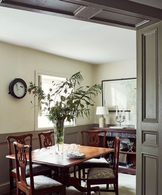 Traditional dining room with painted green wall and ceiling paneling, dark dining table with four matching chairs, plant in center of table, wooden cabinet with table lamp and candelabra and framed map